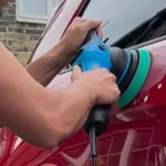 Man using a dual-action rotating polisher to polish and correc the paint on a red car.