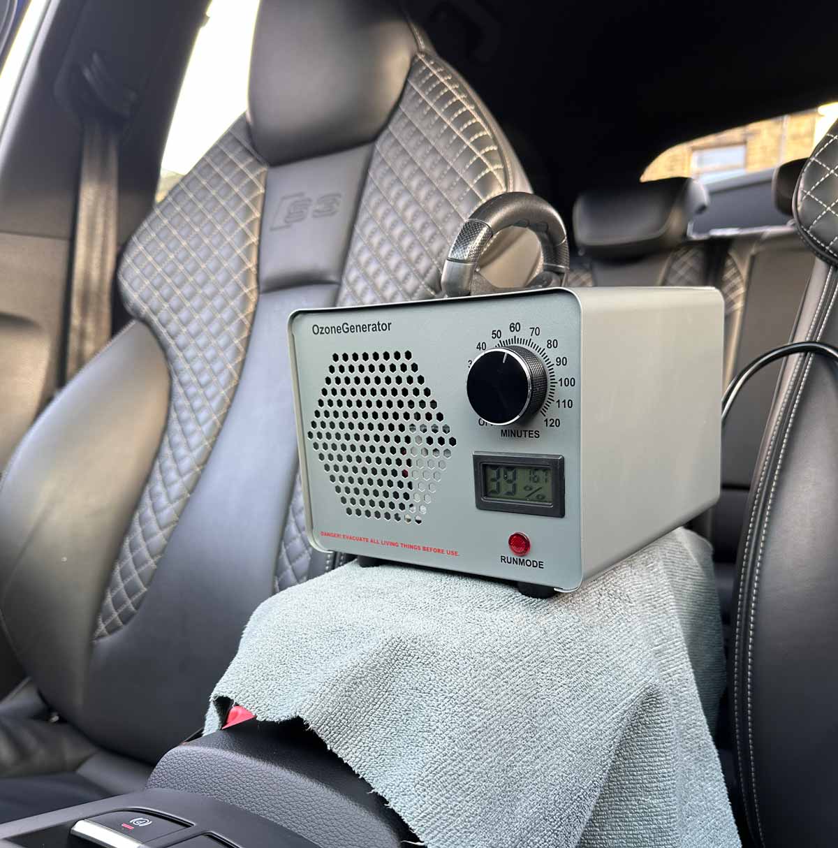 An ozone treatment machine placed inside the interior of an Audi, emitting ozone to neutralise odours and sanitise the vehicle, set against a clean and professional car detailing environment.